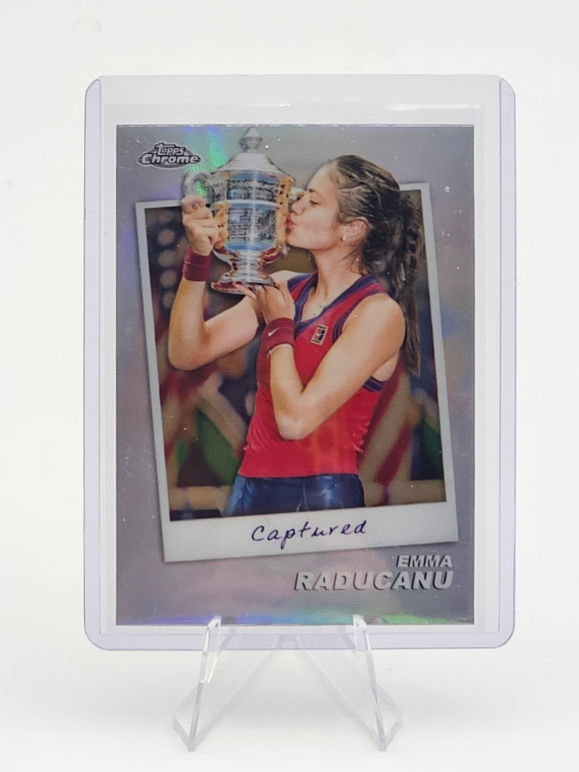 Trading card of Emma Raducanu holding a trophy on a white background